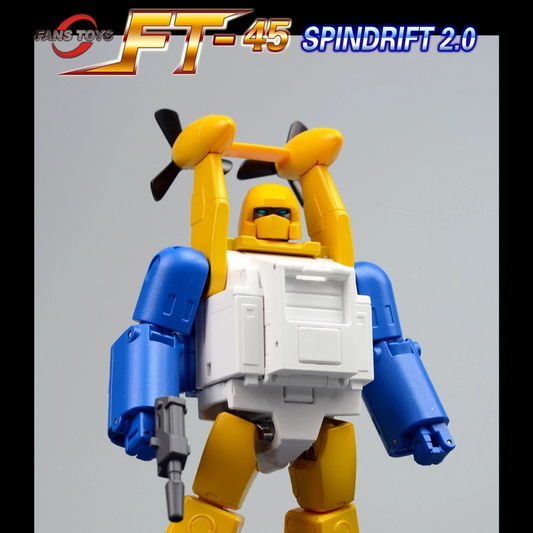 A toy robot figure in blue, yellow, and white stands on gray rubble against a plain light gray background. The figure has a yellow head and arms, blue arms and legs, and a white chest panel.