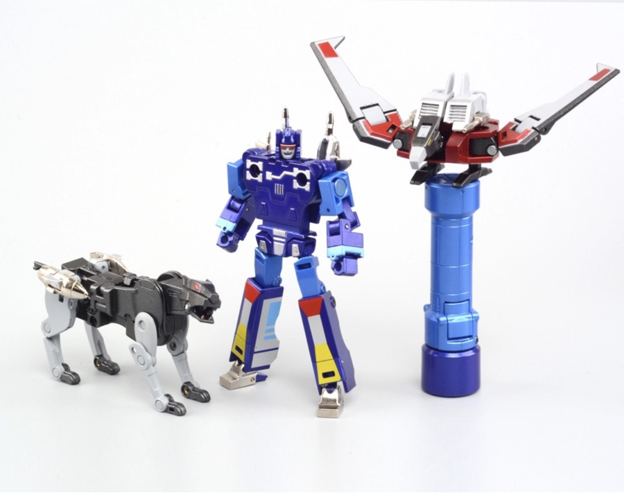 Transformers toy set from Robot Paradise featuring a blue robot figure, a black-and-white dog-like mini figure, a blue-and-black tower structure, and an orange-and-gray box component, all displayed on a white background with the model name RP-01B.